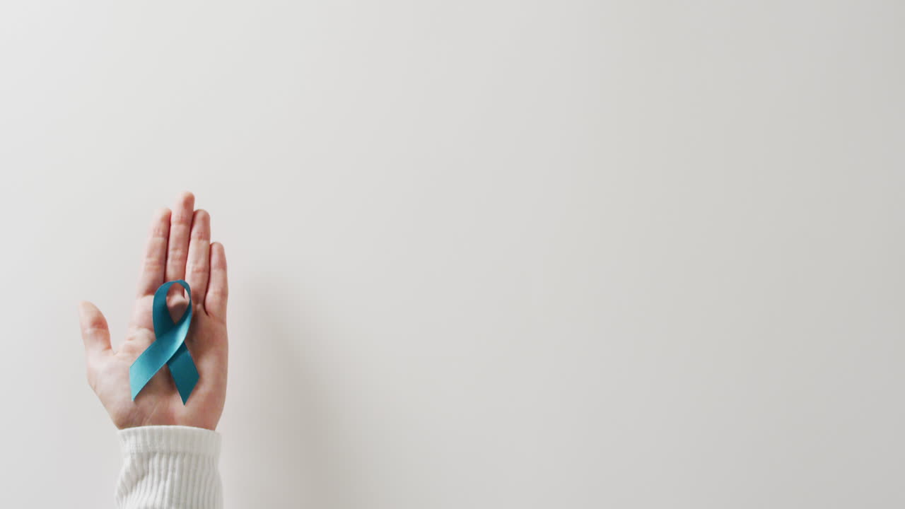 video de la mano sosteniendo una cinta azul de concienciación sobre el cáncer de ovario sobre un fondo blanco con espacio para copiar.