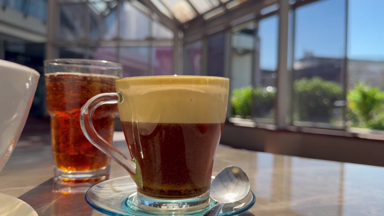 Primo piano del tradizionale caffè all'uovo vietnamita (cà phê trứng) servito accanto a un bicchiere di tè freddo, che mostra la ricca e cremosa schiuma di tuorlo d'uovo stratificata sopra il caffè scuro.