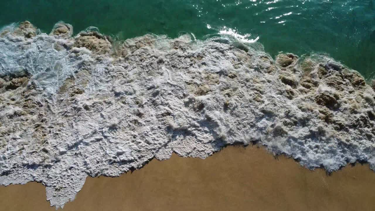 вид с воздуха на волны, разбивающиеся о песчаный пляж