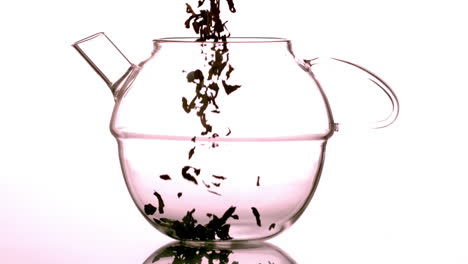 loose herbal tea falling into glass teapot