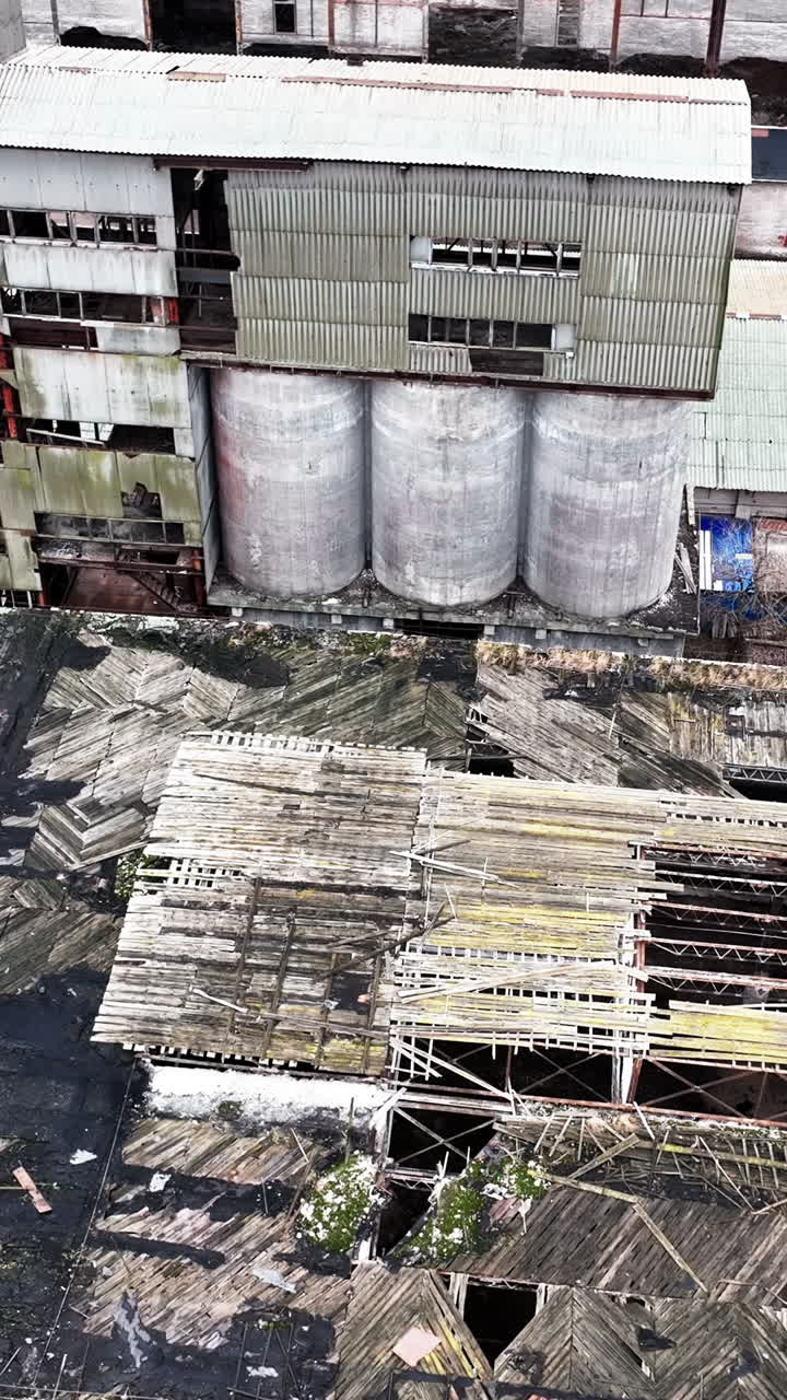 Warehouses of an old plant. Aerial perspective on the wrecked roof of a long empty warehouse in the industrial area. Vertical video
