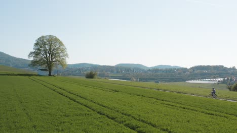 Drone---Aerial-panorama-shot-of-al-lonely-chapel-on-a-field-with-grass-with-a-bike-rider-and-a-road-with-panorama-of-the-seven-mountains---Siebengebirge-25p