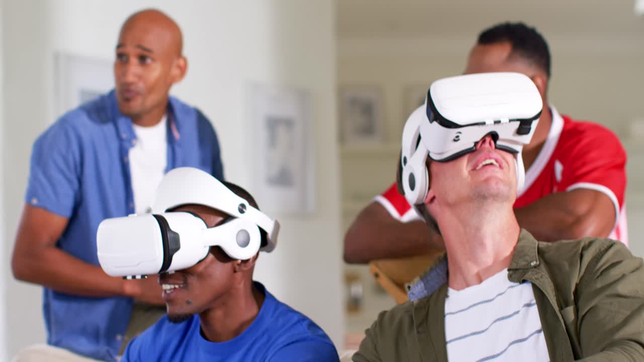 Amici maschi di diverse etnie che giocano alla VR indossando visori bianchi, ridendo e tenendo in mano i controller a casa.