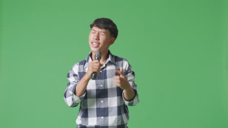 young asian teen boy holding a microphone and singing on the the green screen background