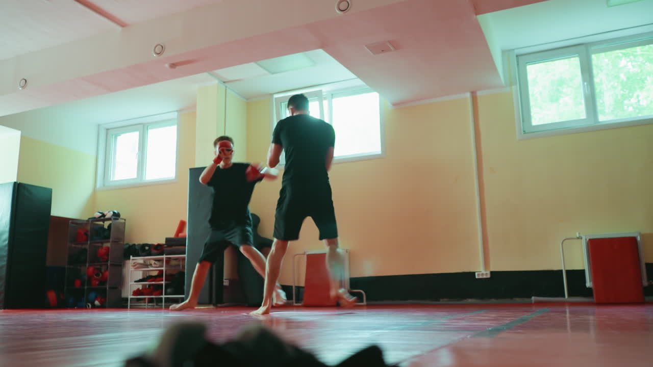 Two fighters sparring in gym on red mat, barefoot, wearing gloves, practicing martial arts stance, preparing for punches, focusing on agility, strength, balance speed, combat performance under natural light