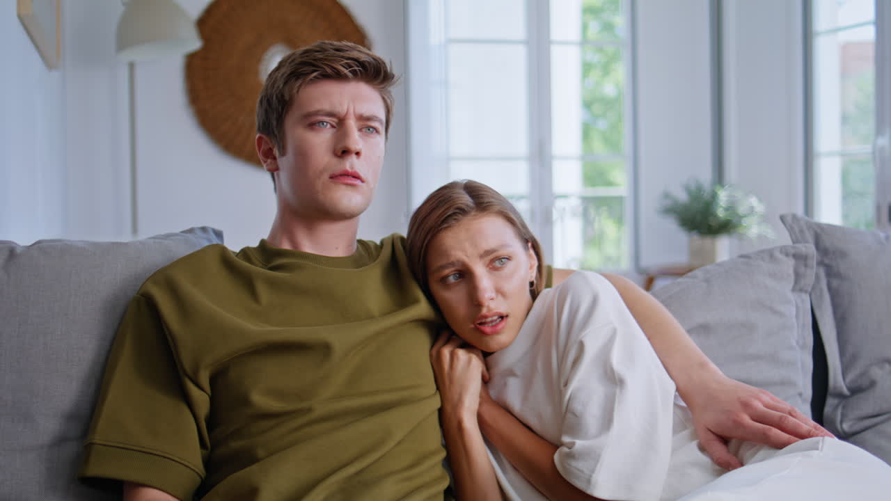 Young family watching television thriller at home closeup. Scared girlfriend