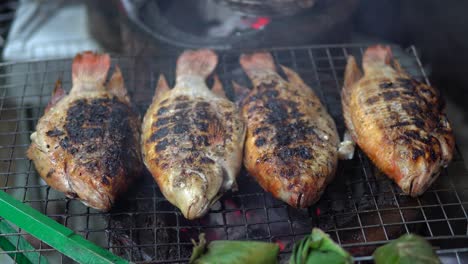 whole sea fish is being cooked on metal grid grill at the street near restaurant in thailand