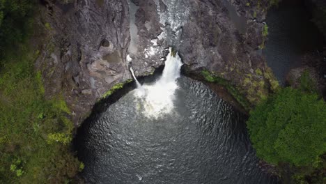 4k cinematic overhead drone shot of a waterfall pouring over a lava rock cliff near the rainforest in hilo on the big island of hawaii