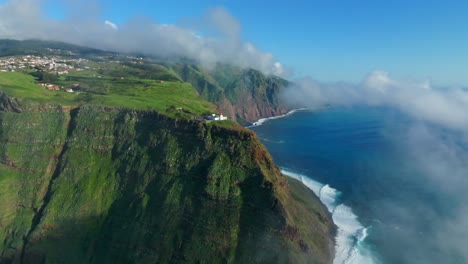 Misty-clouds-scattered-below-rocky-cliff-of-lighthouse-in-Ponta-do-Pargo-Maderia,-Portugal