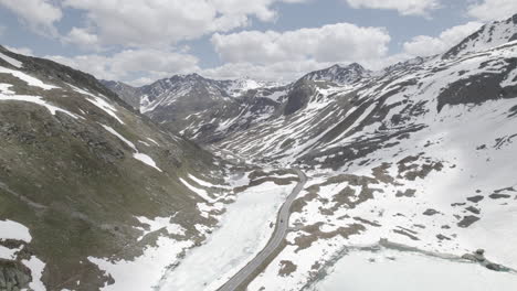 Drone-shot-flying-over-a-single-road-in-between-snow-mountains-at-the-Fluela-Pass-in-Switzerland-on-a-cloudy-and-cold-day-with-clear-sight-LOG