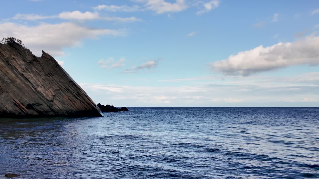 Rocky coastline meeting calm blue sea under a bright sky, showcasing serene coastal scenery and natural beauty