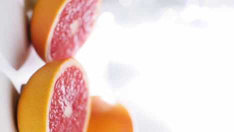 vertical video of grapefruit halves on a white reflected surface, dolly in slow motion shot