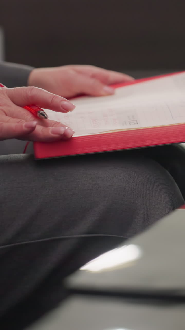Close-up of businesswoman's hand placing red smartphone on top of red notebooks and papers in corporate office. Professional workspace with organized items reflecting productivity and focus