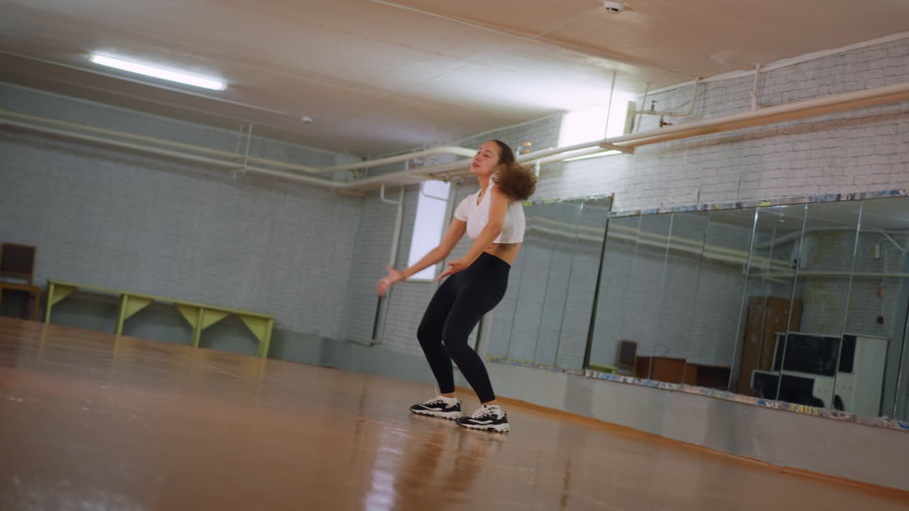 Girl in white top and black leggings dancing inside fitness studio, moving body with energy and rhythm, showing focus, graceful confident performance, and expressive movement on polished floor