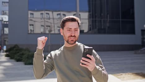 excited business man looking on smartphone screen celebrating victory outside