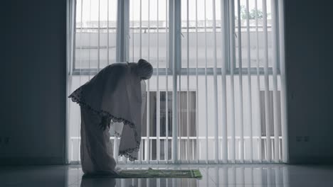 side view of old woman doing salat near window