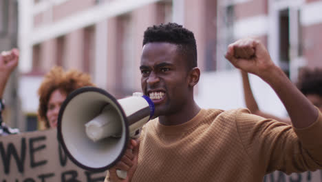 african american man shouting using megaphone with other people holding placards during protest