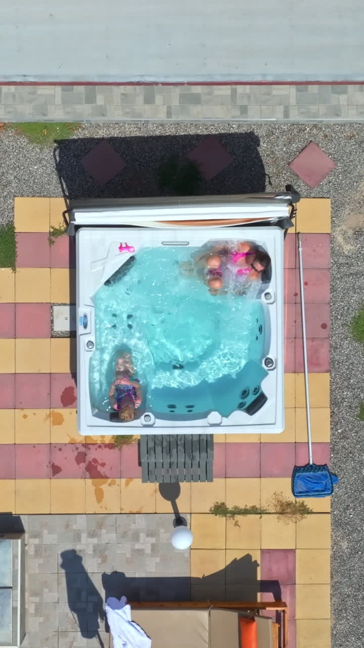 Vertical drone shot above a mother and daughter relaxing in a jacuzzi, sunny day