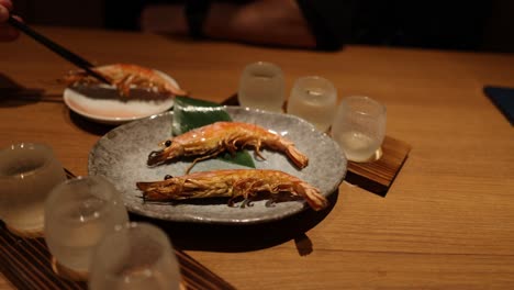 Hands serving grilled shrimp on a plate with tongs