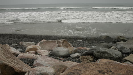 a uhd wide-angle shot captures a quiet rocky beach on an overcast morning, with soft gray light, textured stones, and gentle waves creating a serene, moody, and contemplative coastal scene.