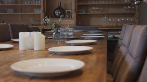 una mujer colocando cubiertos en una gran mesa de comedor de madera