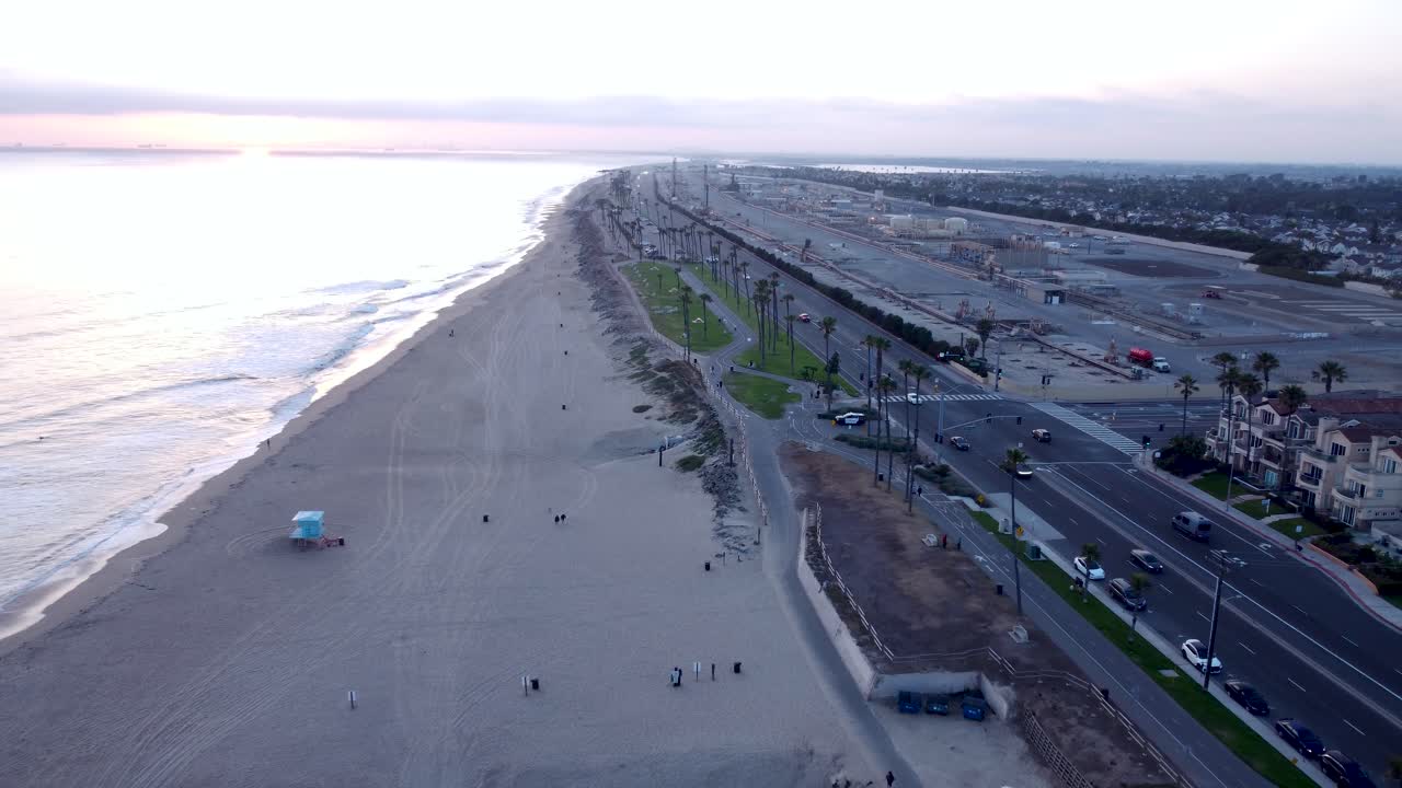 Huntington Beach California, Pacific Coast Highway 1. Auto che passano accanto a palme tropicali al tramonto. Calda luce dell'ora d'oro e calme onde dell'oceano. Contea di Orange, California