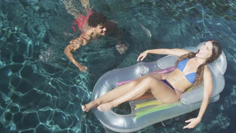 feliz pareja biracial con inflable en la piscina en un día soleado
