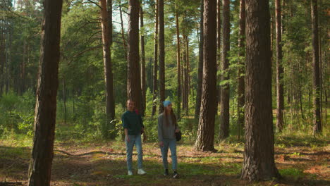 two sisters walking through sunlit forest, one with red backpack and cloth, other with blue headscarf gazing into the distance, sunlight filters through trees