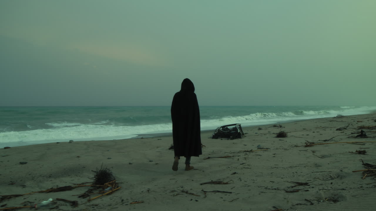 Silhouette di un uomo con mantello cammina vicino all'oceano inquinato nella notte del terrore.
