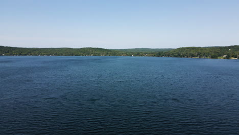 Stunning-blue-sky-reflects-on-ripple-windy-lake-surrounded-by-thin-green-band-of-rolling-hills