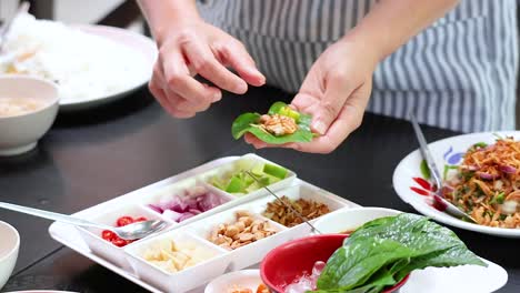 hands assembling traditional thai miang kham leaf wraps with ingredients