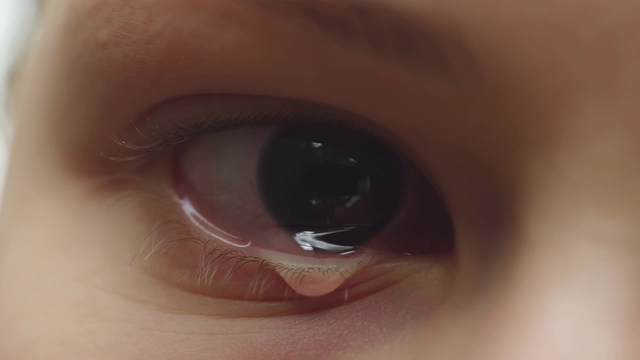 Makronærbilde som viser et menneskeøye delvis åpent, med blank hornhinne, reflekterende høydepunkter, tåredråpe som dannes ved nedre øyelokkskant, iris litt til høyre for midten, og en rolig kontemplativ stemning.