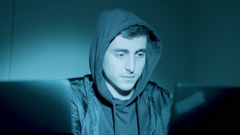 young caucasian man sitting at night in front of laptop screen and hacking