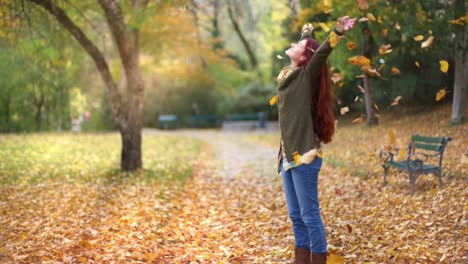 cámara lenta: hermosa joven pelirroja parada en un parque en otoño con hojas cayendo a su alrededor