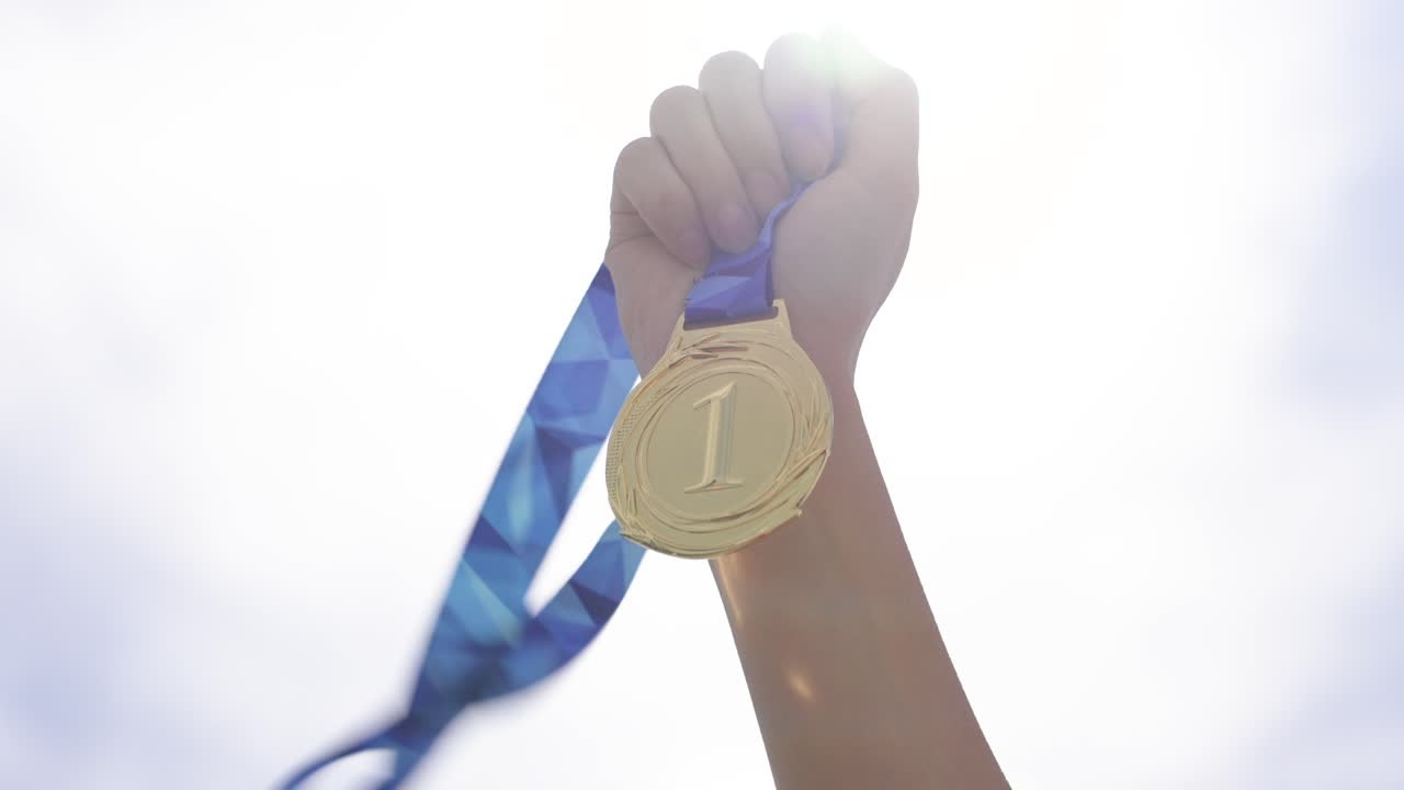 Close-up of hand holding a victory medal against outdoor sky background. Concept of achievement, success, winning, motivation, reward, and recognition for effort and excellence
