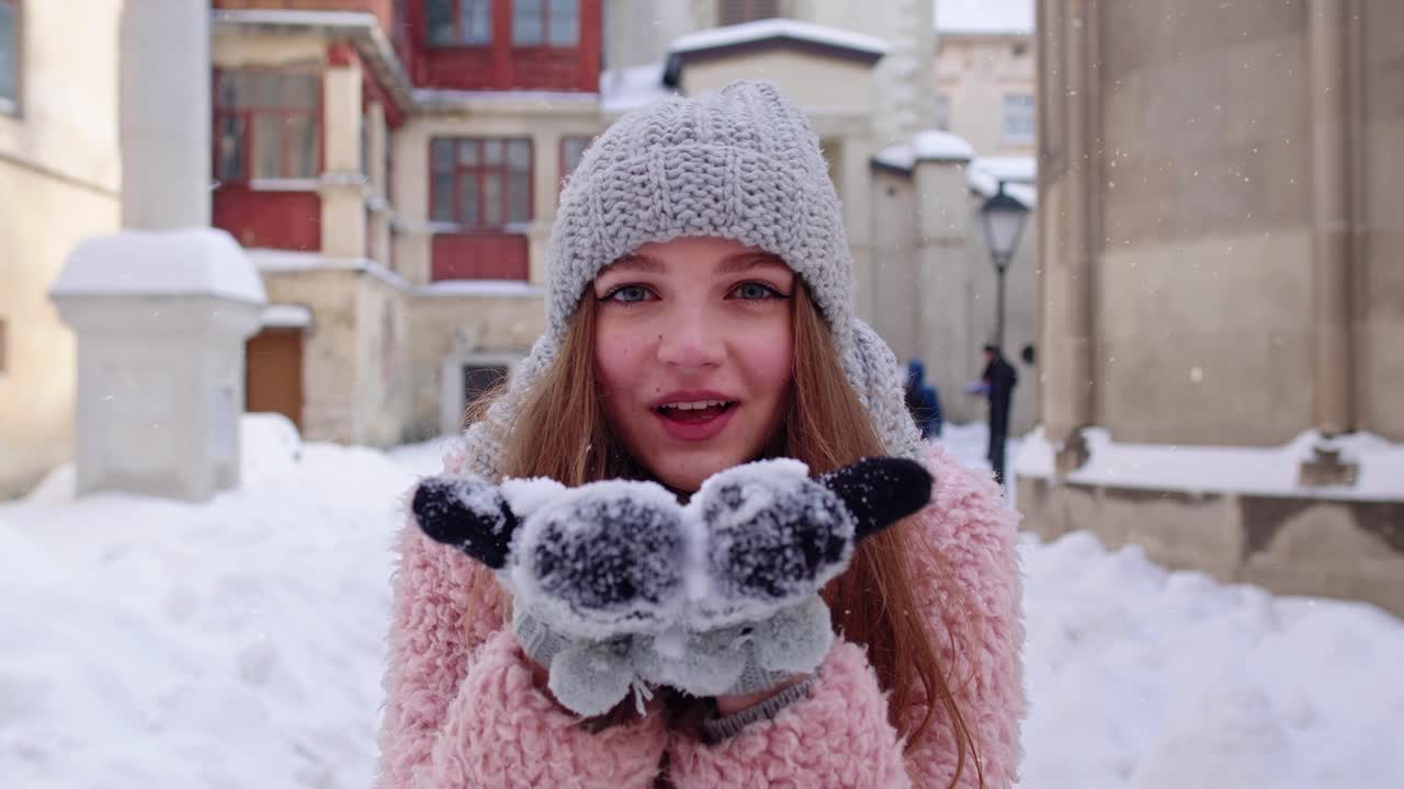 joven turista viajera mostrando nieve en las manos palmas a la cámara y soplar en la calle de la ciudad