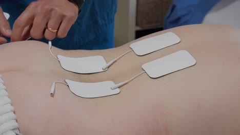 hands attaching white electrodes on woman's skin for electrical stimulation