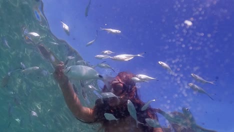 perspectiva subacuática inusual de una niña fuera del agua de mar que alimenta a la escuela de peces