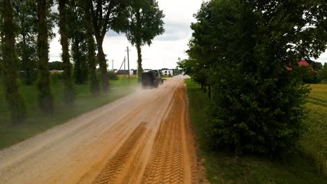 shot of tractor driving on a dirt road with trees and bright sky