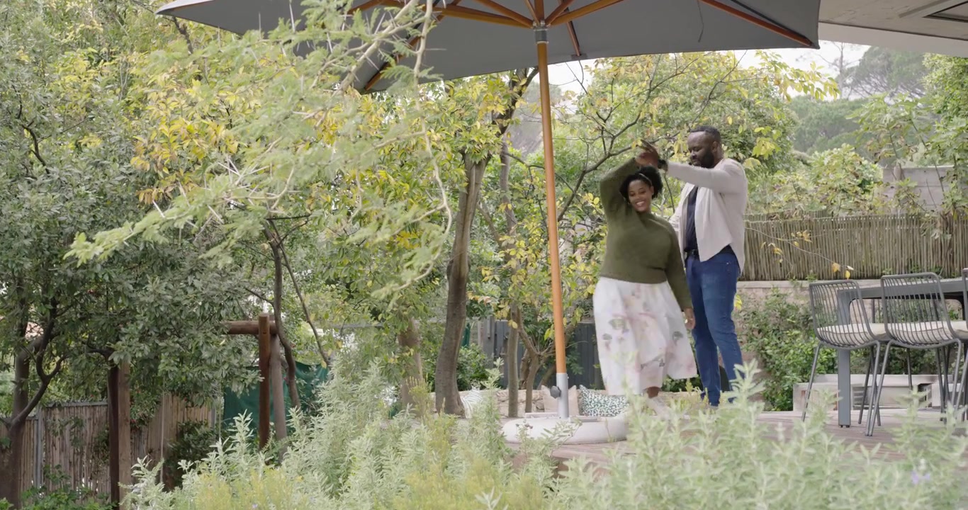 African American couple dancing on deck, woman pulling man, twirling under umbrella, showing love
