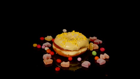 yellow funny surprised glazed donut with sprinkles, striped caramel candies, colorful dragee with raisins or peanuts inside rotate on black background