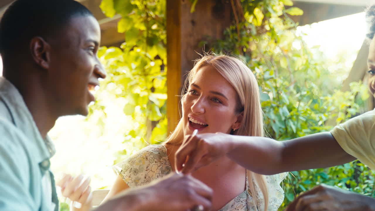 Primo piano di un gruppo di amici multiculturale sorridenti che consumano un pasto insieme all'aperto a casa.