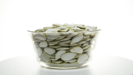 glass bowl full of raw pumpkin seeds rotating on isolated white studio background