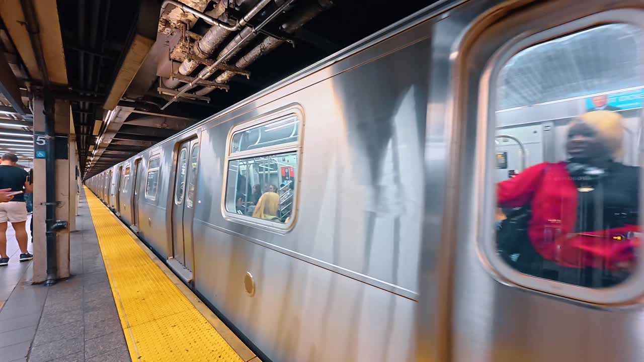 New York, USA, 9 agosto 2025: Effetto mosso di un treno della metropolitana che arriva alla banchina della stazione. Treno della metropolitana argentato in rapido movimento in una stazione sotterranea con linea di sicurezza gialla sulla banchina a New York.