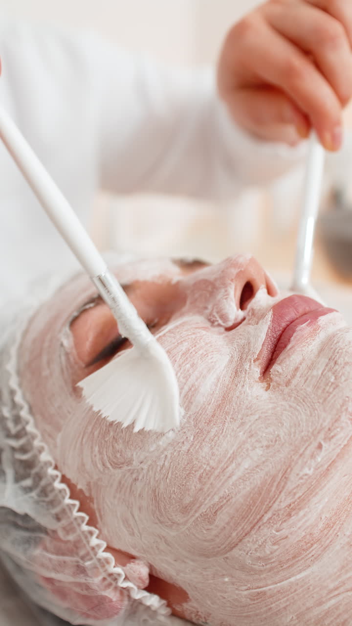 Enzyme therapy beautician applying moisturizing medical cream on middleaged woman face with brushes