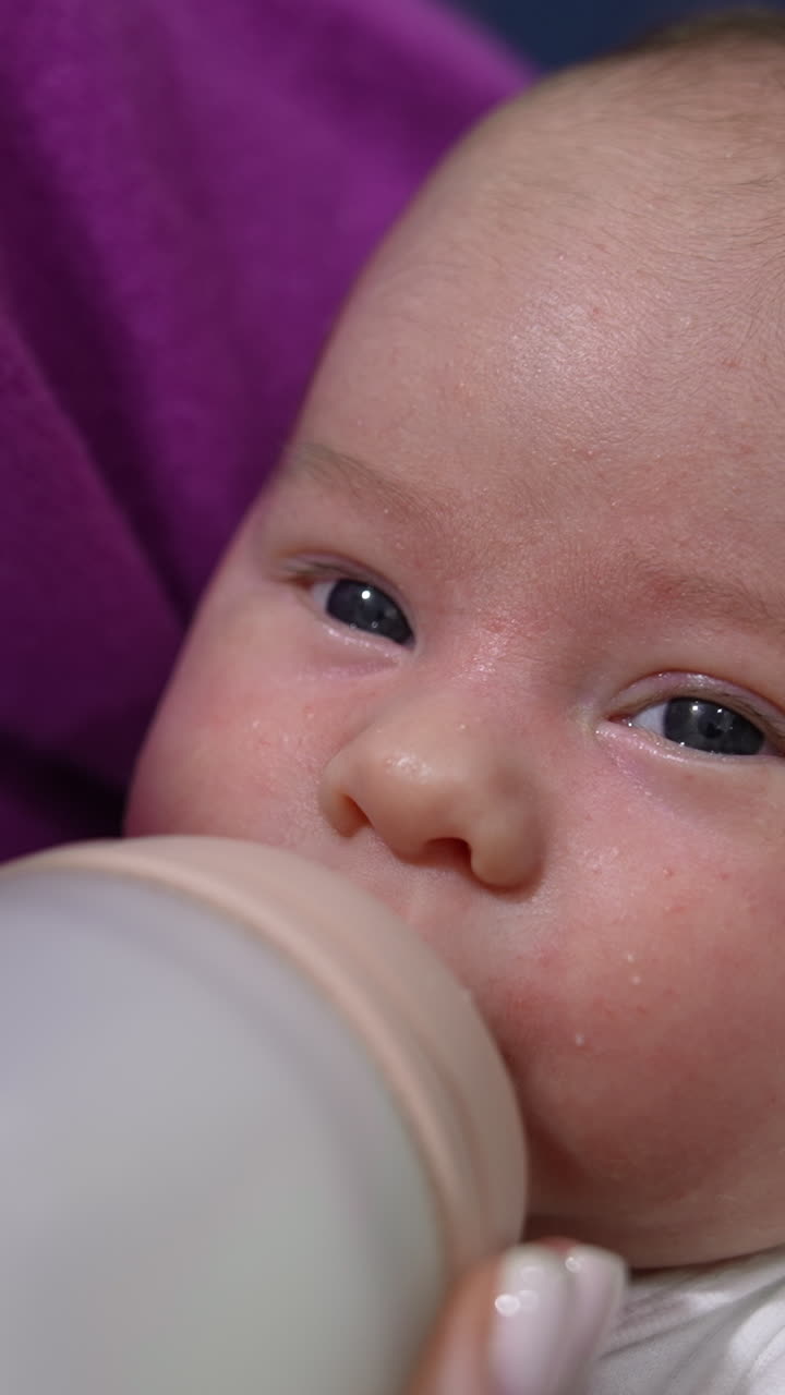 Adorable newborn baby being fed from the bottle. Mother holding her child in arms and feeding it from the bottle. Close up. Vertical video