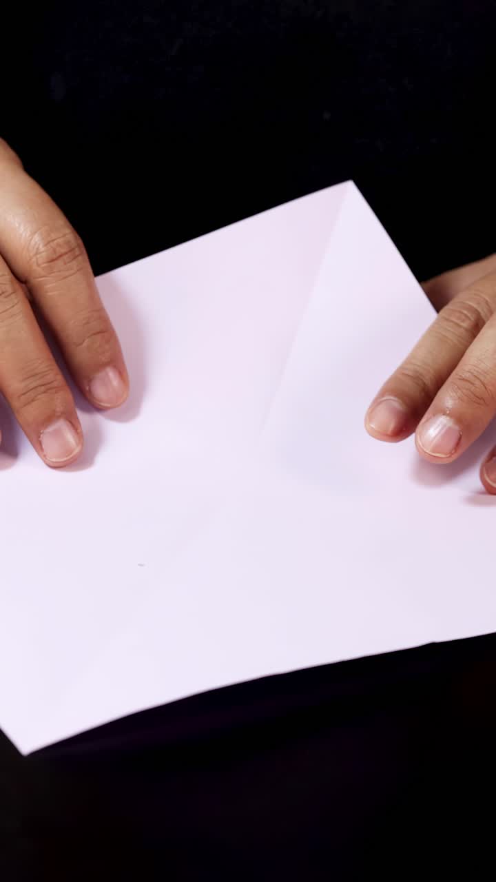 Mani adulte piegano con cura carta bianca su un tavolo nero sotto un'illuminazione morbida e uniforme, vista ravvicinata
