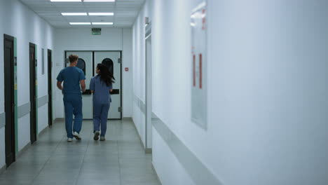 unknown doctor nurse moving down hallway back view. surgeon consulting woman.