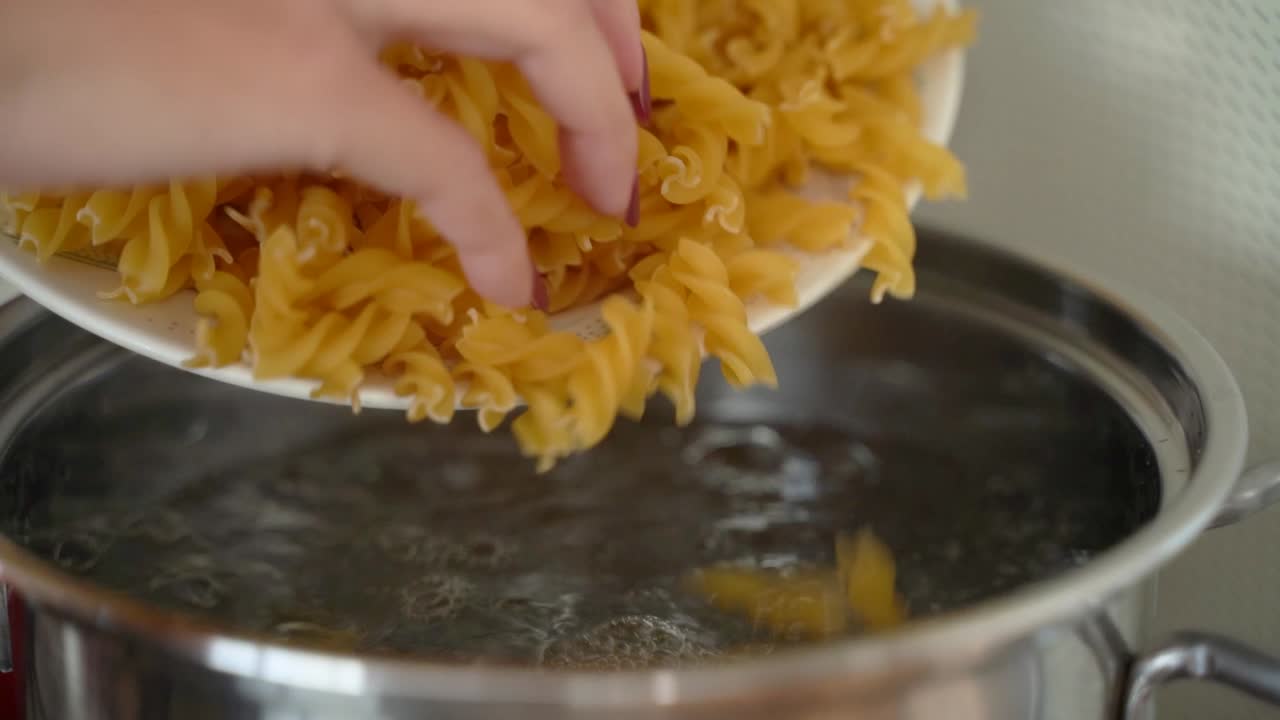 mano femenina tirando pasta tortiglioni en agua hervida
