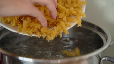 female hand throwing tortiglioni pasta into boiled water